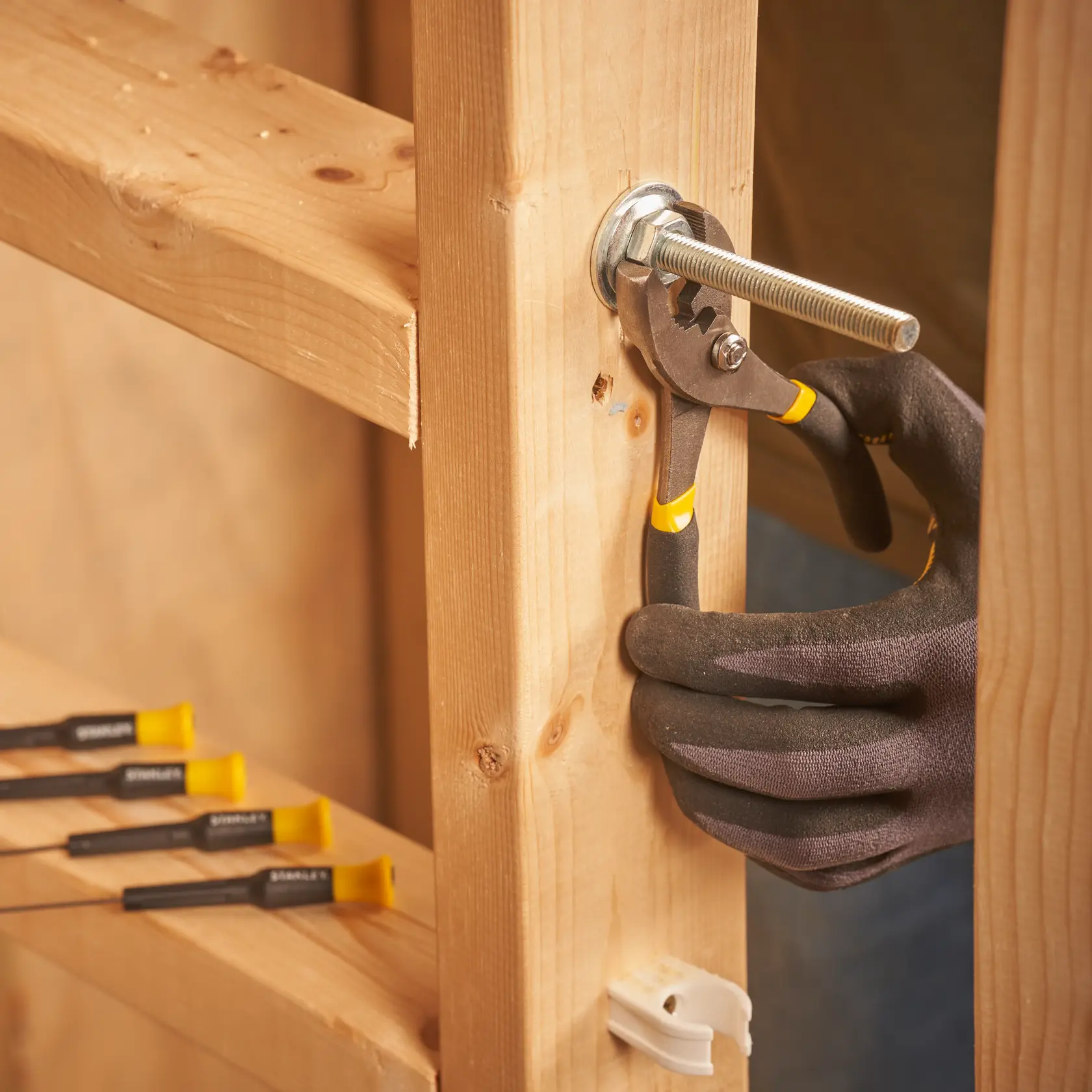 STANLEY STMT0-74101 pliers tightening bolt on wood, close-up, black-yellow handle, workshop setting.