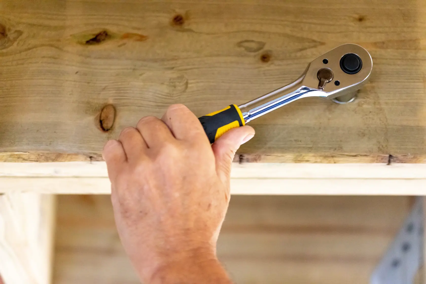 STANLEY STMT82665-0 Knarrenschlüssel an Holz, Nahaufnahme einer Hand mit dem Werkzeug.