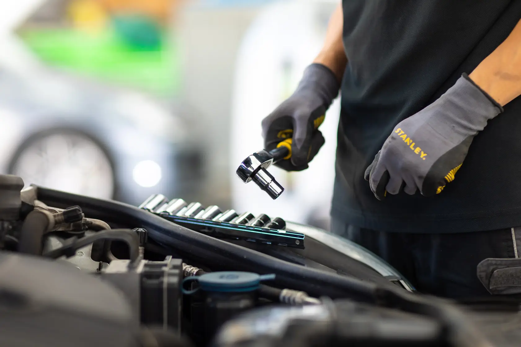 Stanley STMT82666-0 mechanic using ratchet and socket set next to car engine, close-up view.