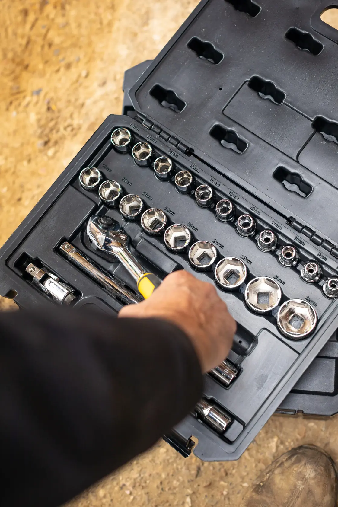 STANLEY STMT82830-1 socket set with ratchet, sockets, and accessories in black case, hand reaching for tool.