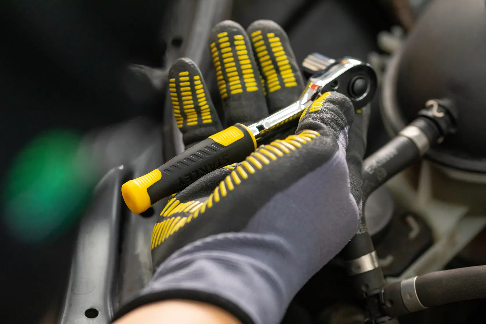 STANLEY STMT82831-1 Ratschen-Schlüssel in behandschuhter Hand, schwarzer und gelber Griff, Automobilbereich.