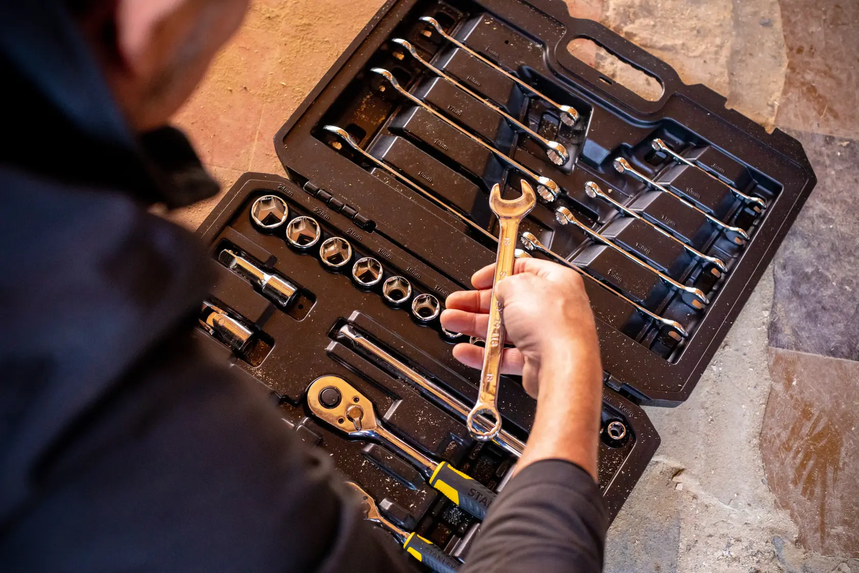 STANLEY STMT82832-1 mechanic tool set with wrenches, sockets, and ratchets, top view, person holding wrench.