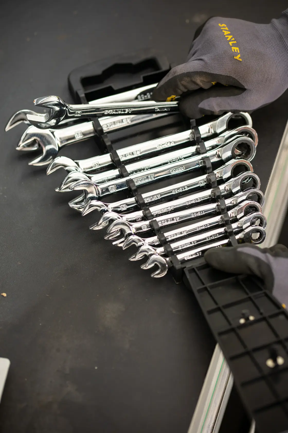 STANLEY STMT82847-0 ratcheting wrench set in holder, chrome finish, shown with gloved hands on black surface.