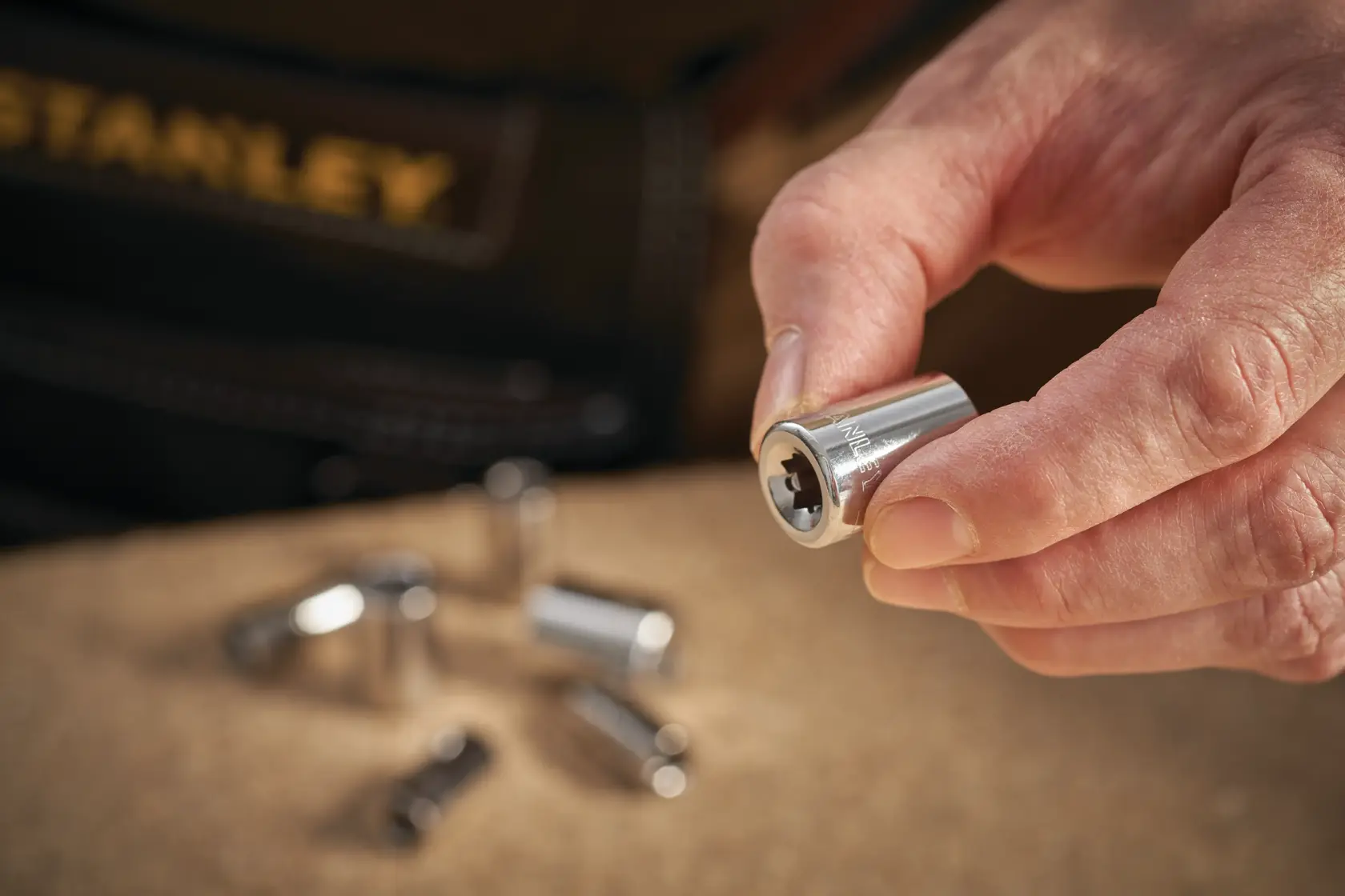 STANLEY STMT86109-0 chrome socket held in hand with other sockets on work surface, close-up photography.