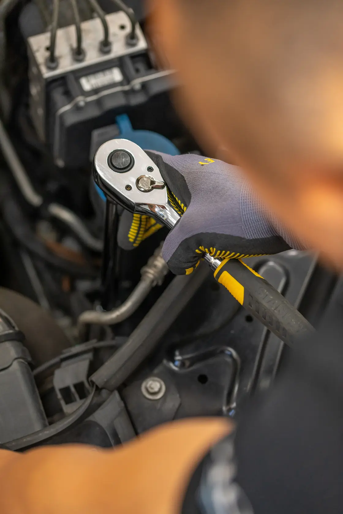 Photo of STANLEY STMT86207-0 ratchet wrench being used on car engine, worker wearing gloves.
