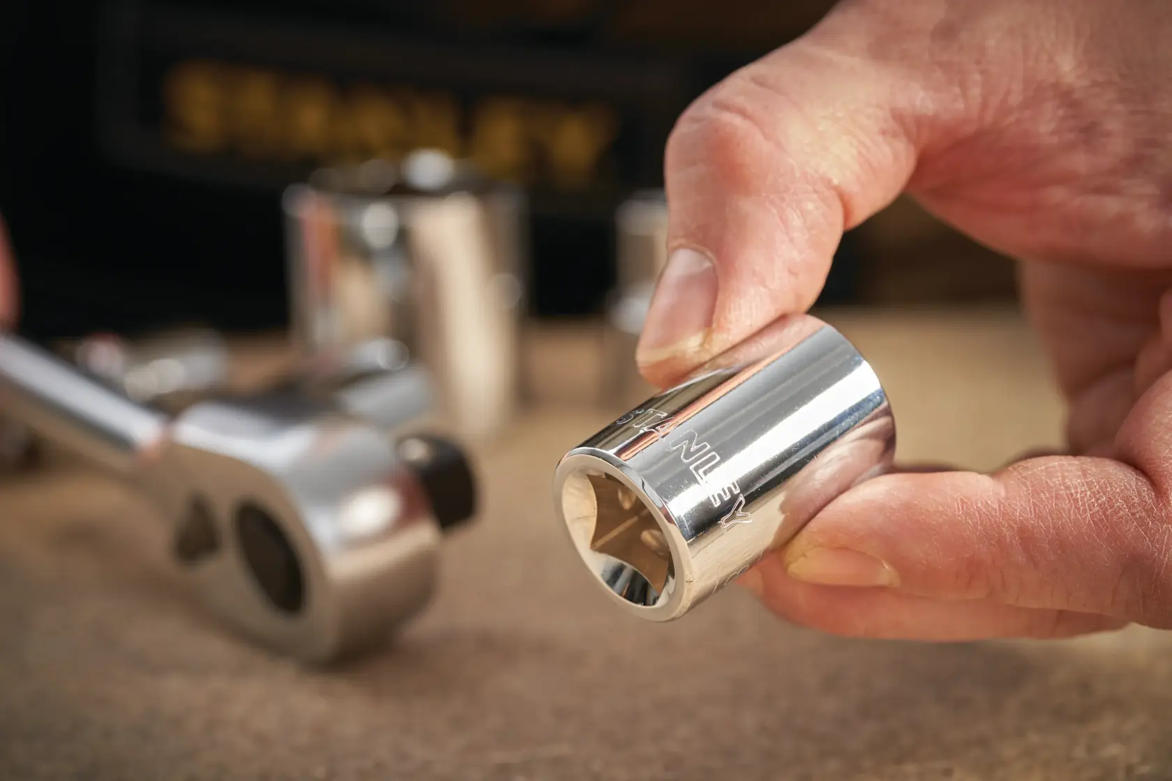 STANLEY STMT86523-0 chrome socket held by hand, ratchet and sockets in background, close-up photography.