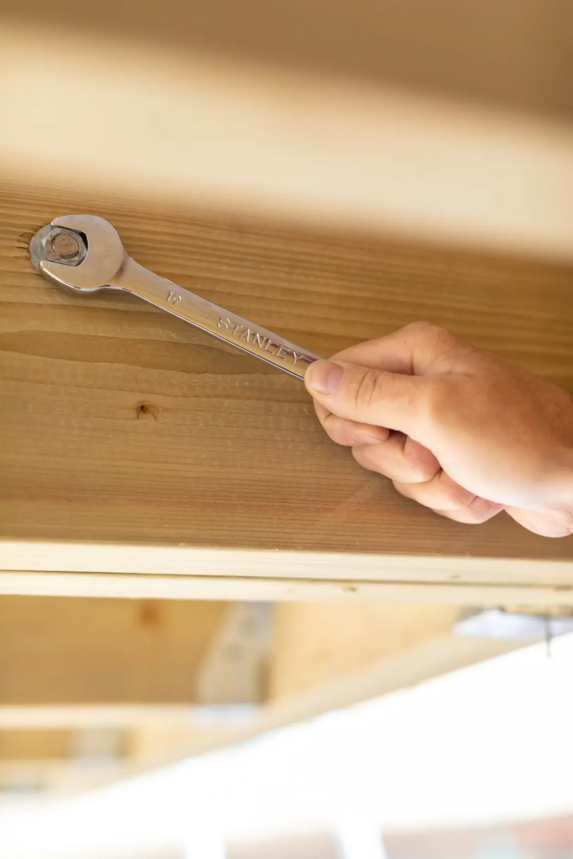 STANLEY STMT89909-0 wrench in use tightening a bolt on wooden beam, side angle photo.