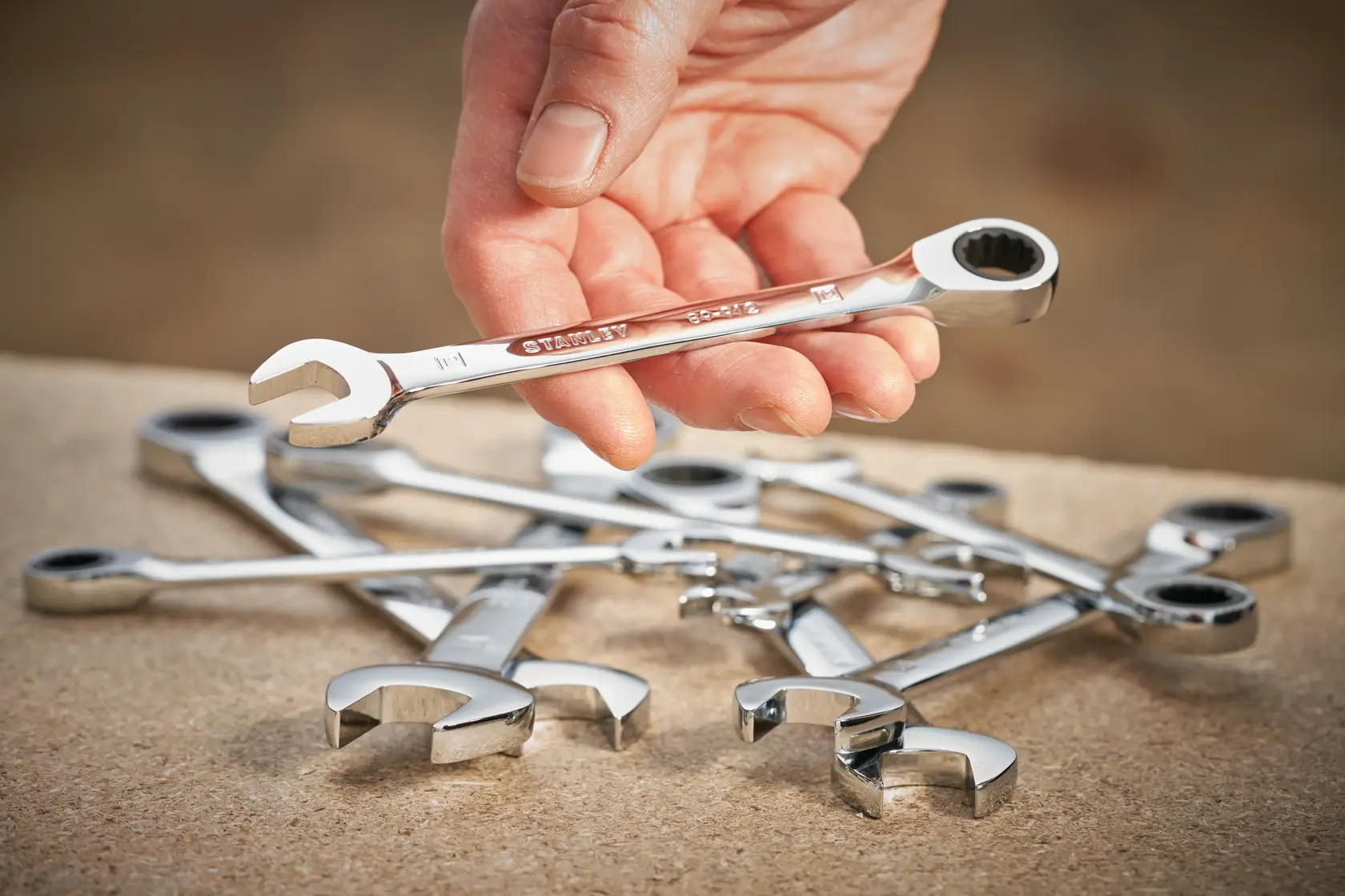 STANLEY STMT89918-0 ratcheting wrench set, chrome finish, hand holding one wrench, shown on work surface.