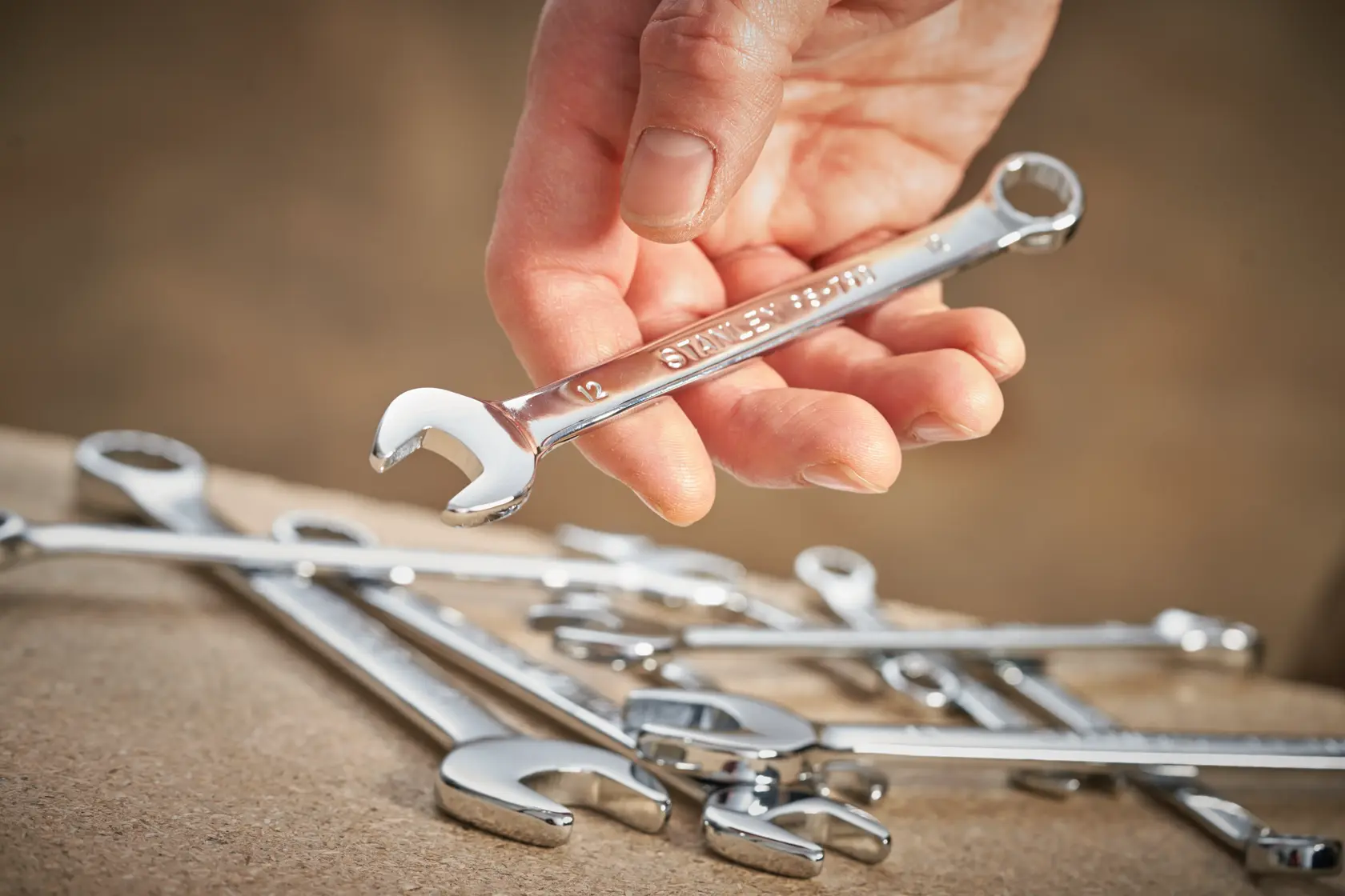 Photo of a hand holding a STANLEY STMT95792-0 combination wrench with other wrenches on a work surface.