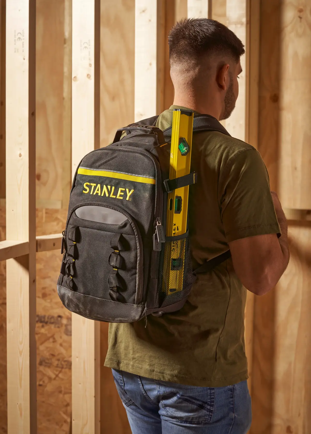 Stanley STST1-72335 schwarz-gelber Rucksack, von einem Mann in einer Werkstatt getragen, mit Wasserwaage.