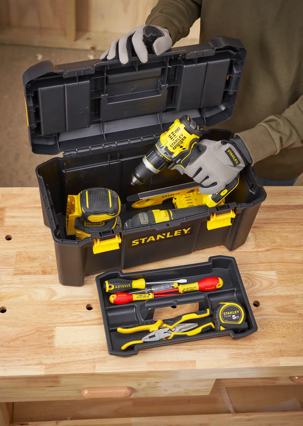 STANLEY STST1-75520 toolbox with yellow-black tools, drill, tape measure, and hand tools on wooden table.