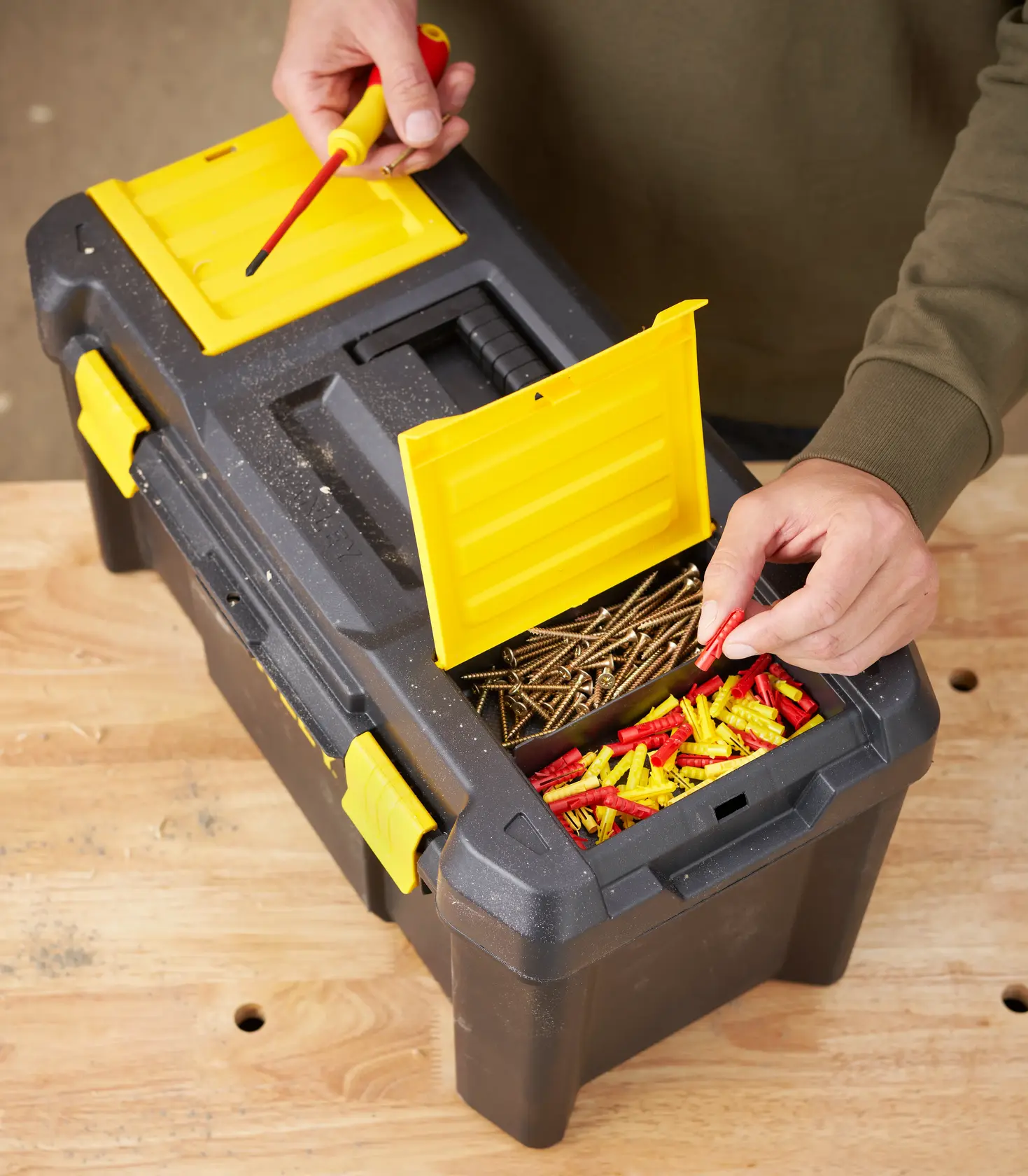 STANLEY STST1-75520 toolbox with yellow latches and open compartment holding screws and wall plugs, top angle.