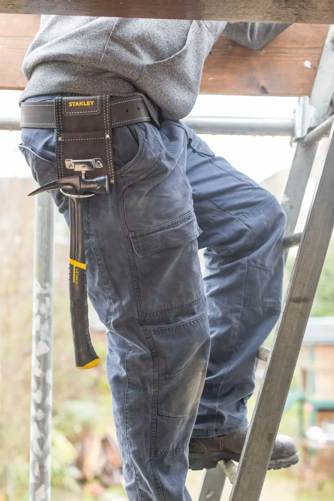 STANLEY STST1-80117 Werkzeuggürteltasche mit Hammer, getragen von Person auf Leiter, Produktfotografie.