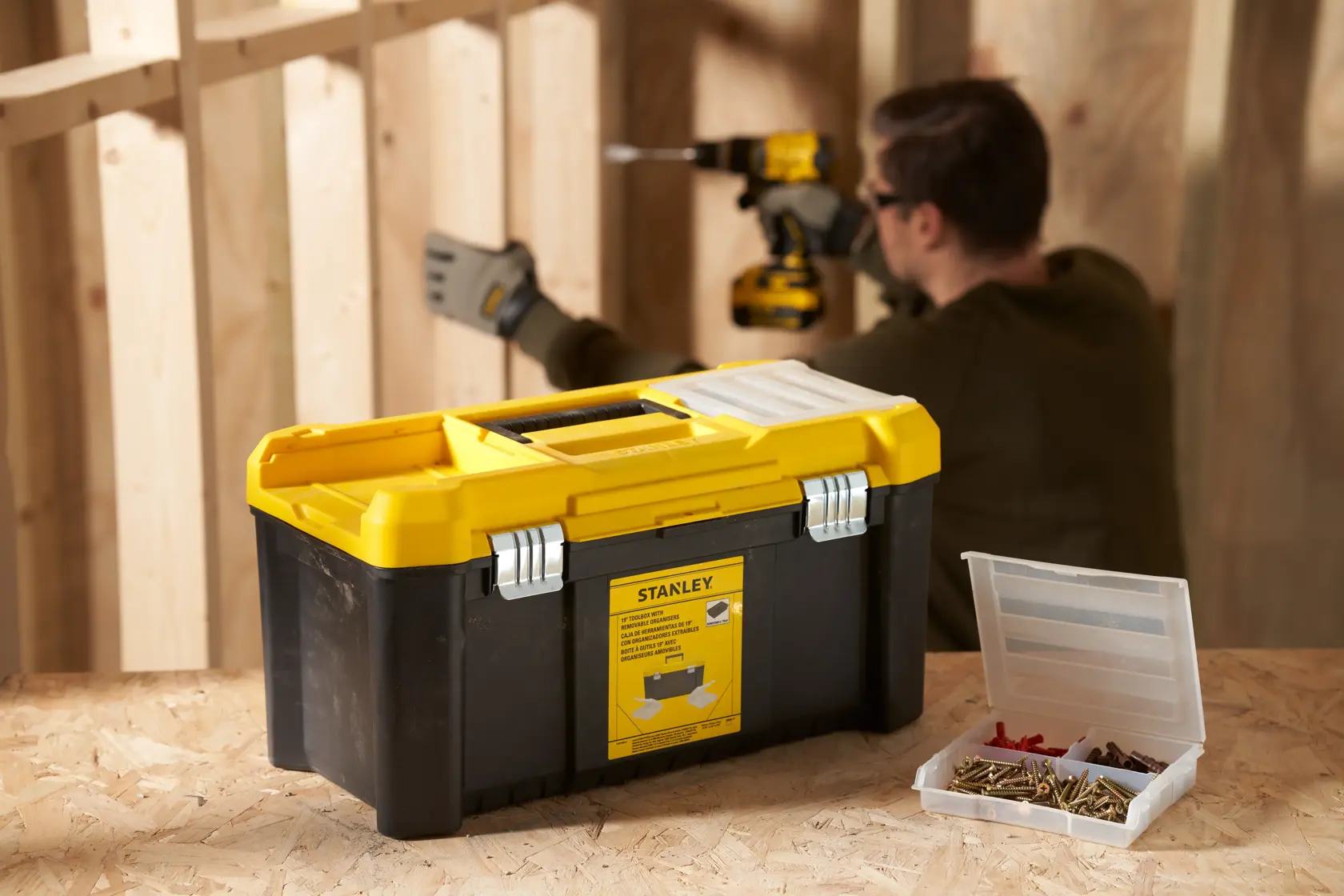 STANLEY STST75787-1 black and yellow toolbox with metal latches on workbench, open parts box nearby, workshop setting.
