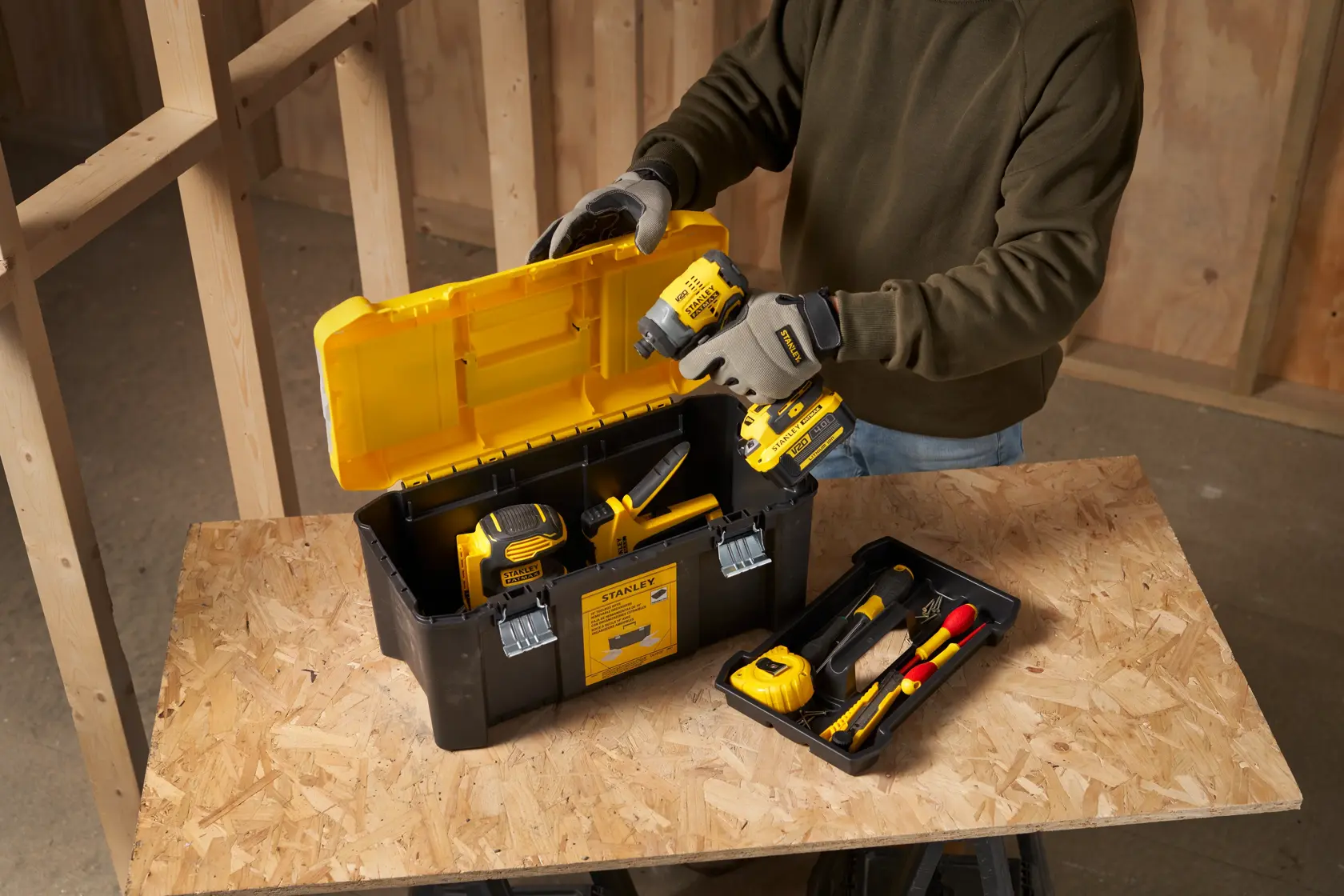 STANLEY STST75787-1 tool box with yellow lid, filled with power tools and accessories on a workbench.