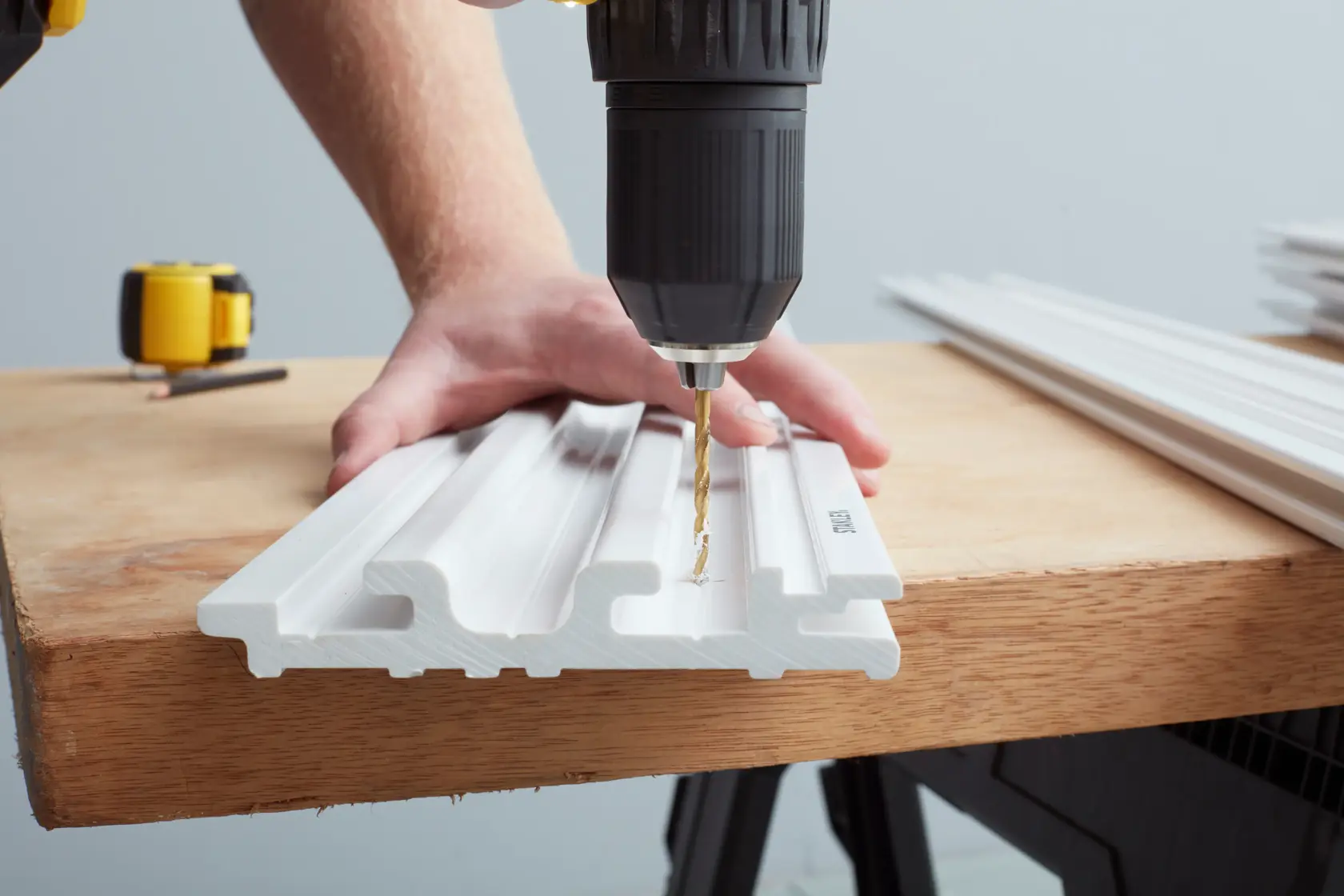 STANLEY STST82602-1 photography of a drill making holes in white plastic moulding on a workbench.