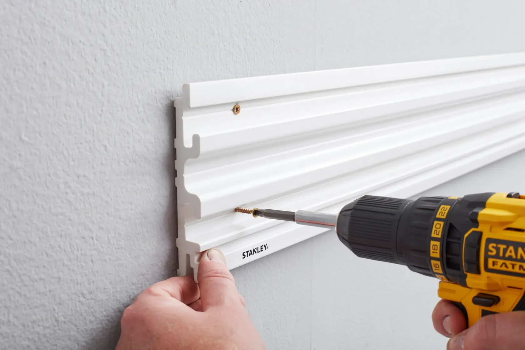 STANLEY STST82602-1 wall-mounted white storage rail, side angle, being installed with power drill.