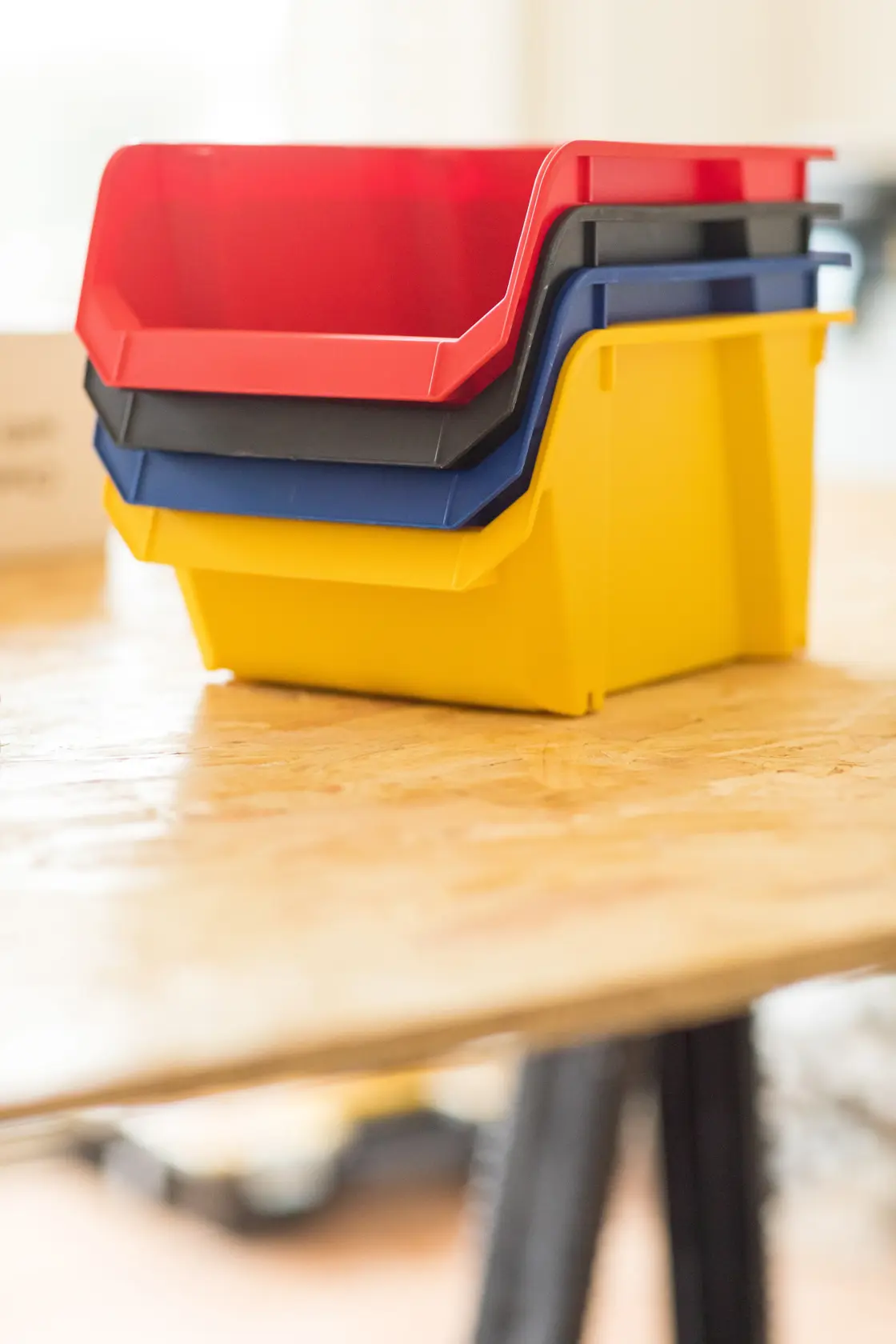 STANLEY STST82739-1 stackable plastic storage bins in red, black, blue, and yellow on a wooden table, side angle.
