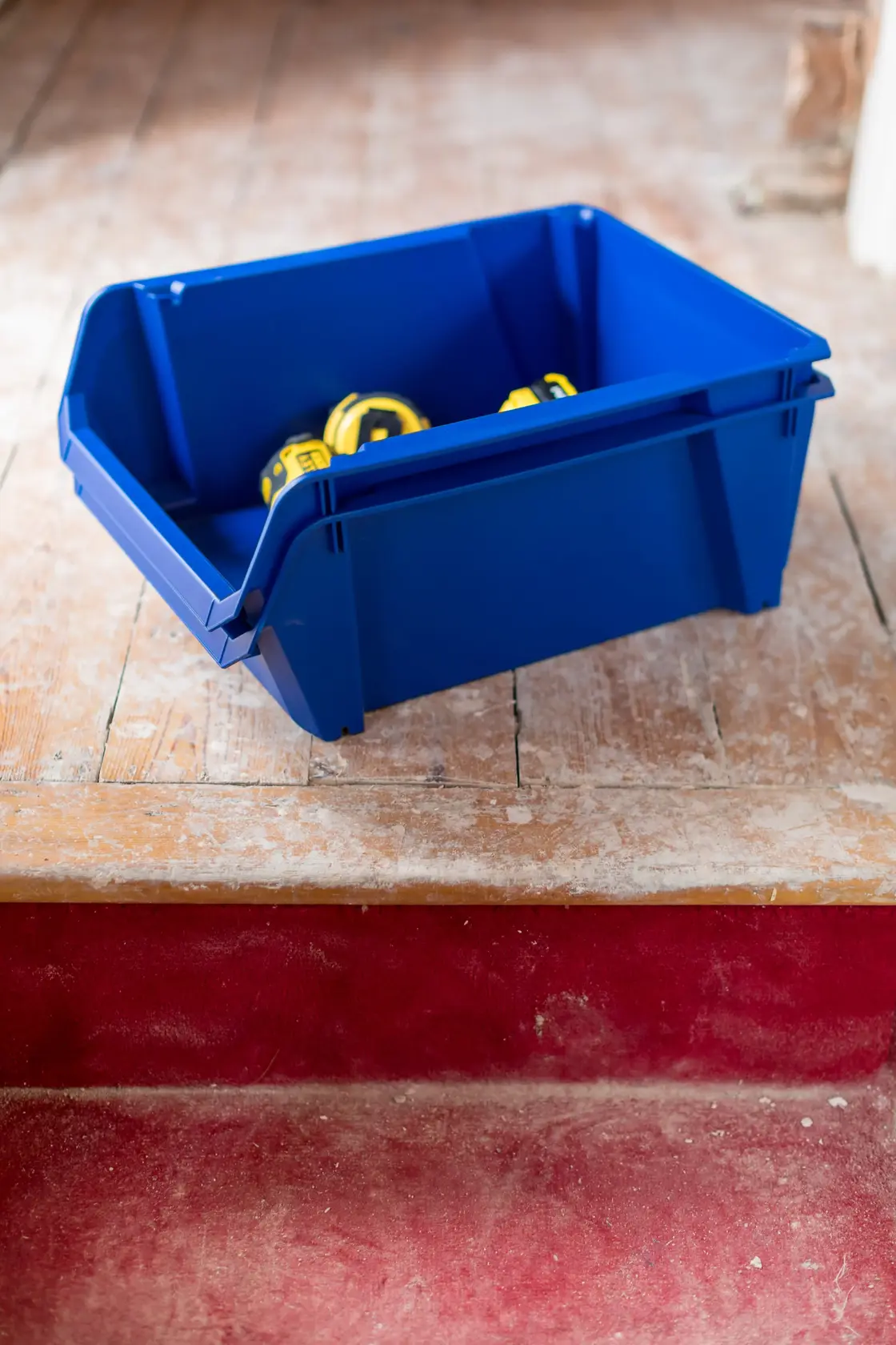 STANLEY STST82746-1 blue storage bin holding yellow tape measures, angled on wooden floor.