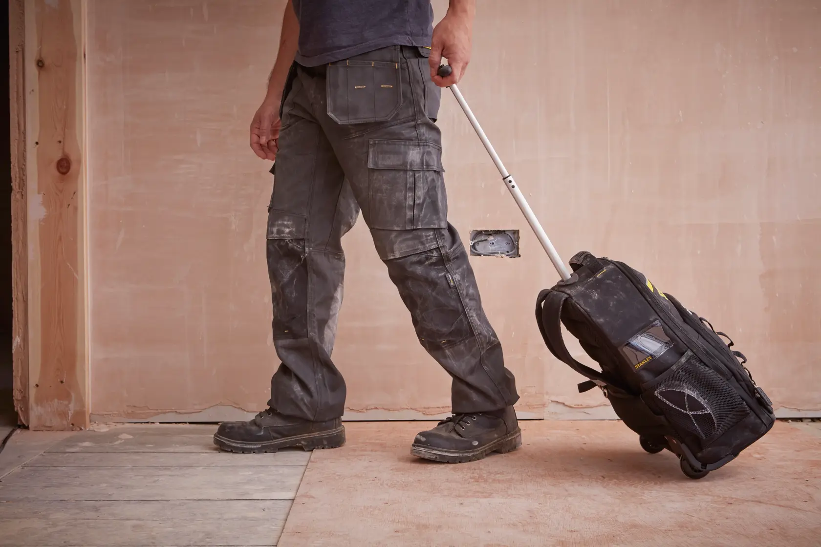 STANLEY STST83307-1 rollender Werkzeugrucksack auf Baustelle, Seitenansicht, schwarz mit gelben Details.