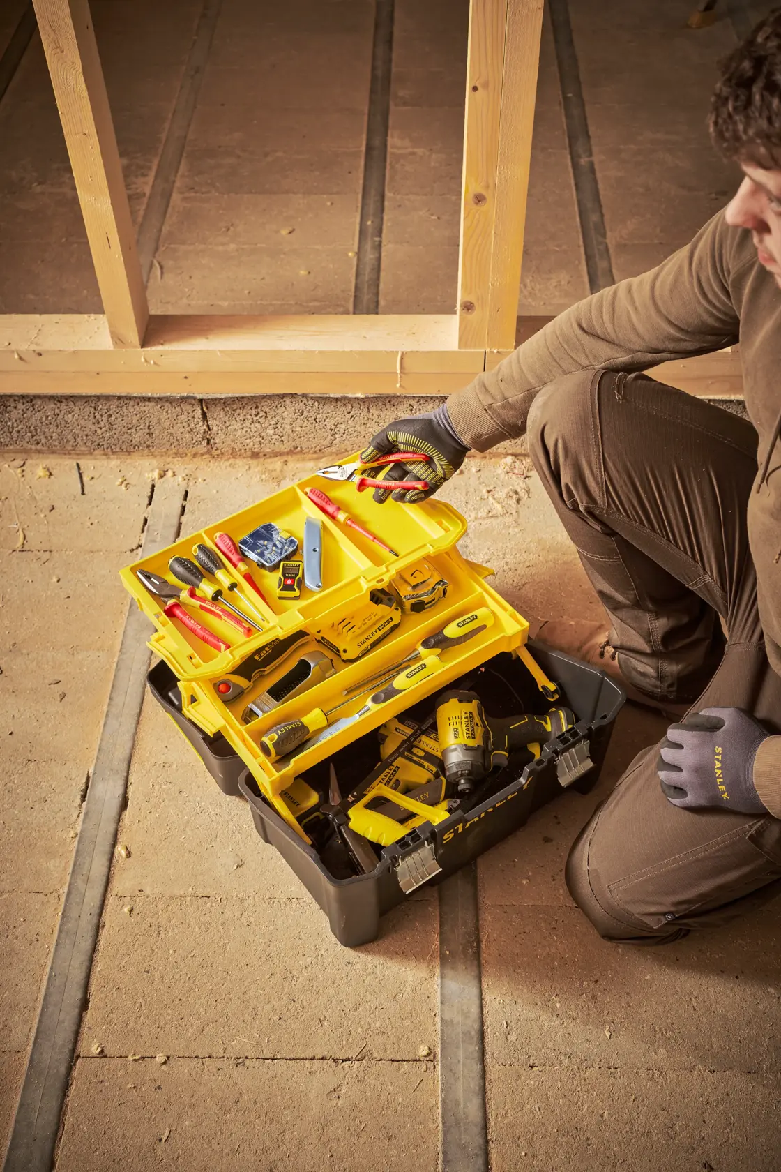 STANLEY STST83397-1 toolbox with yellow trays and assorted tools, photographed at a construction site, top view.