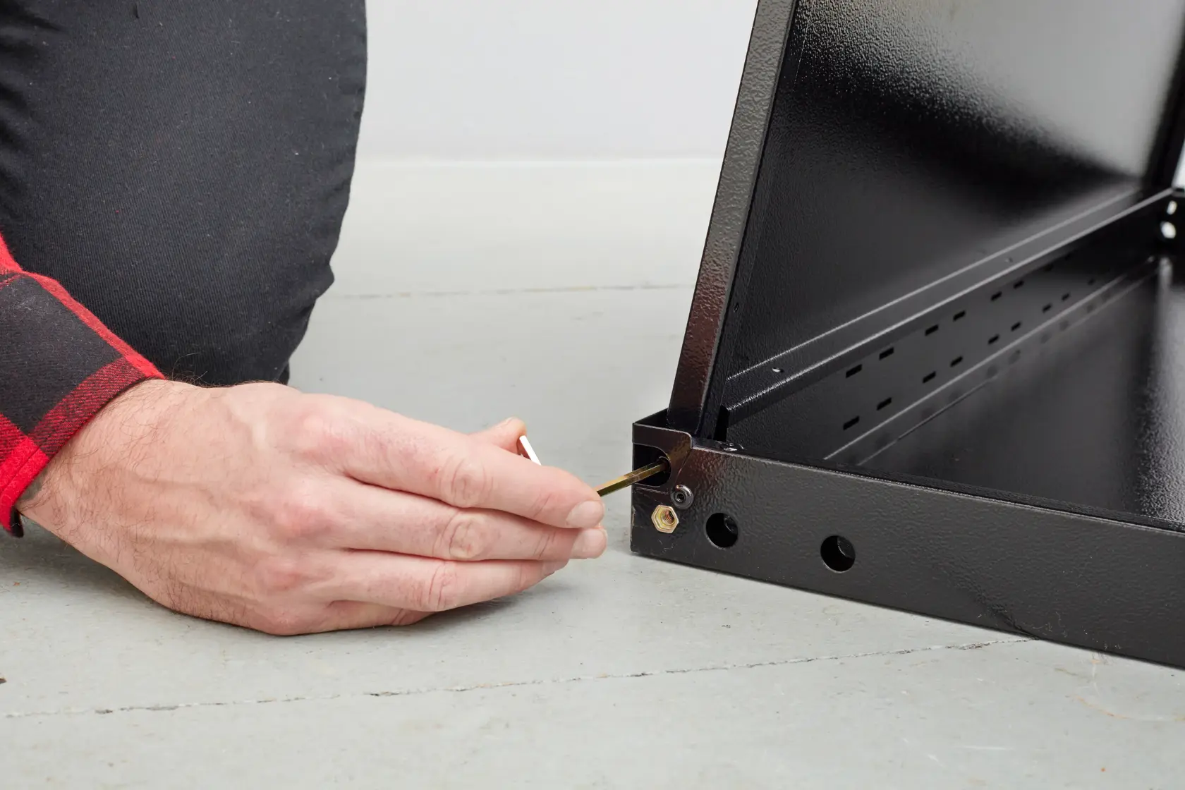 STANLEY STST97595-1 person assembling black metal frame with hex key, close-up on hand and corner joint.