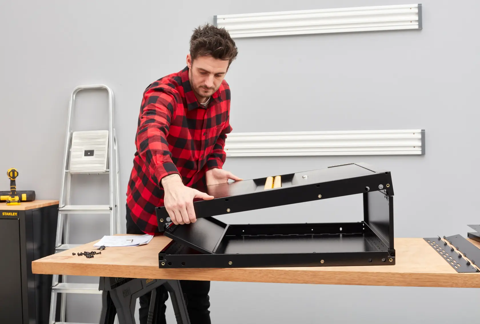 Person assembling a black STANLEY photography accessory on a workbench in a workshop.
