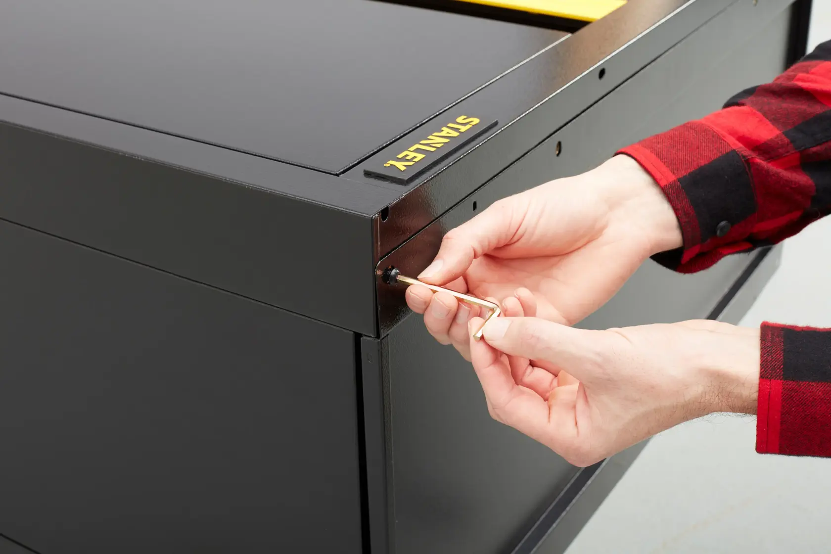 STANLEY STST97957-1 black cabinet, close-up angle, showing hands using Allen key on corner screw.