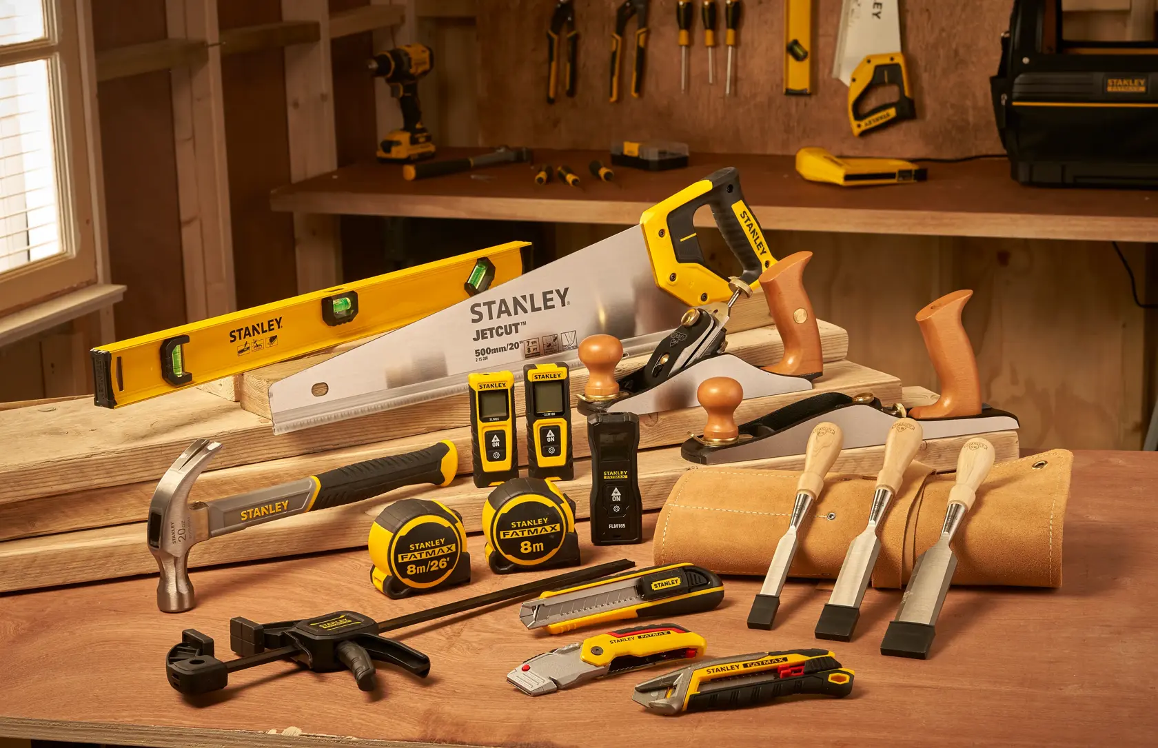 STANLEY STHT77666-0 assortment of hand tools in workshop, including saw, hammer, chisels, tape measures, levels.