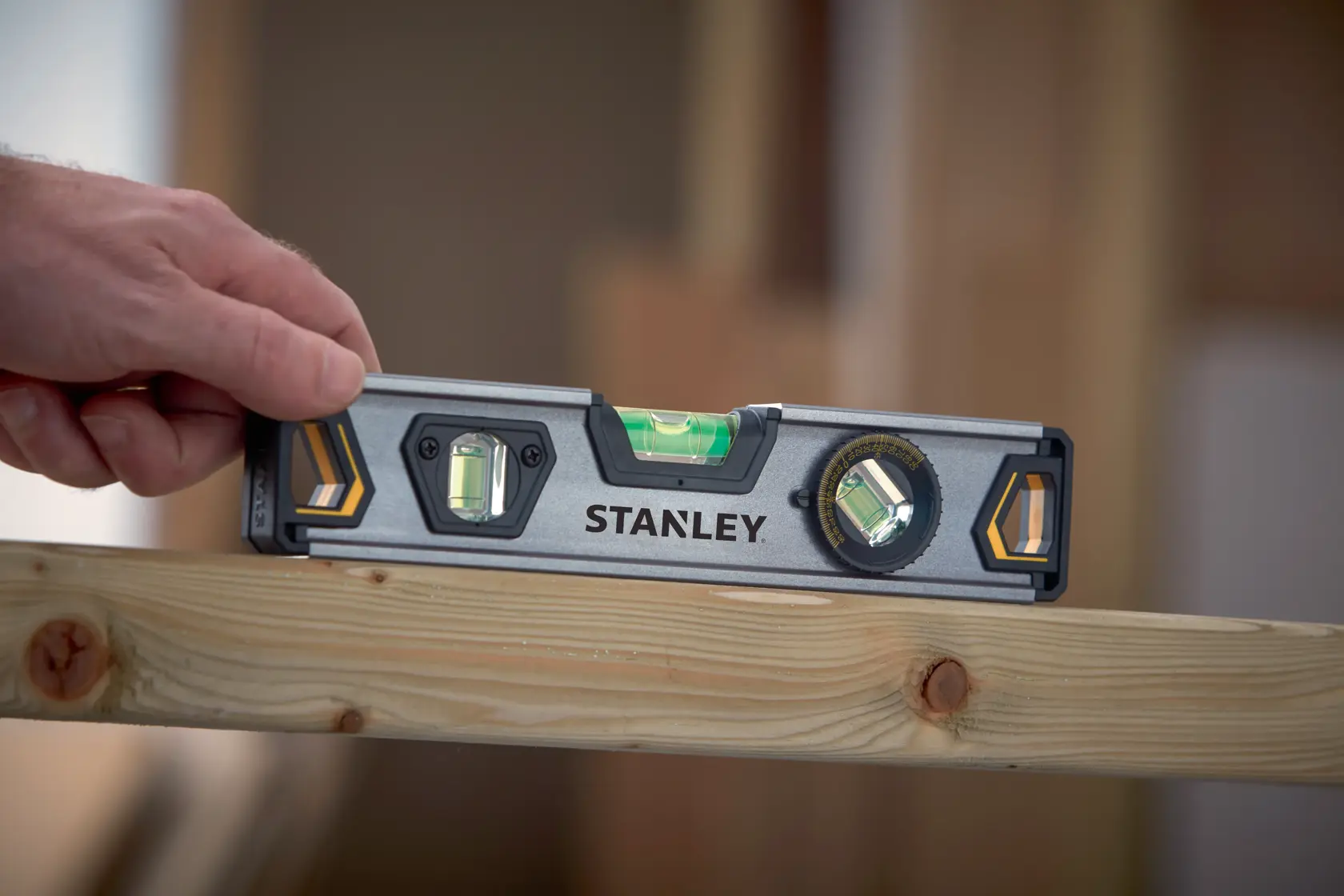 STANLEY XTHT0-42495 spirit level held on wood beam, construction setting, close-up angle.