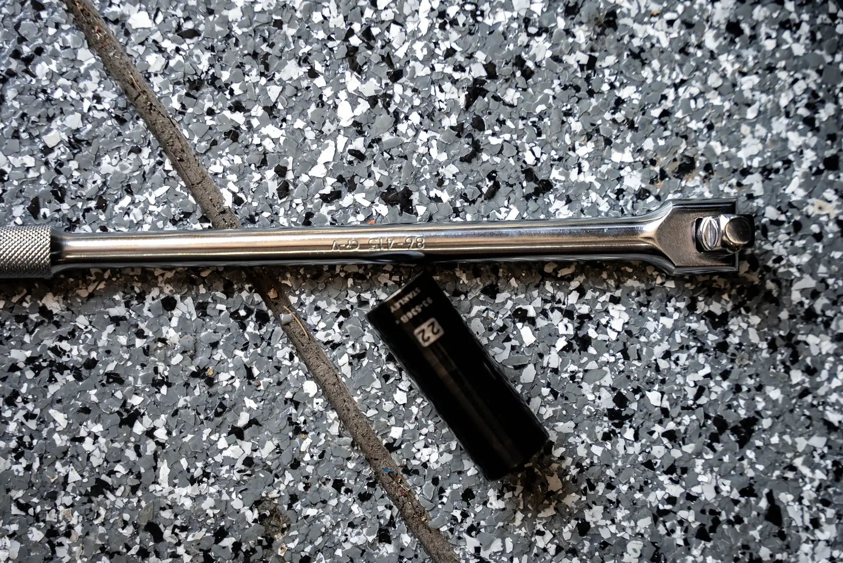 STANLEY STMT17107CCT breaker bar and black socket on speckled gray tile floor, top view.